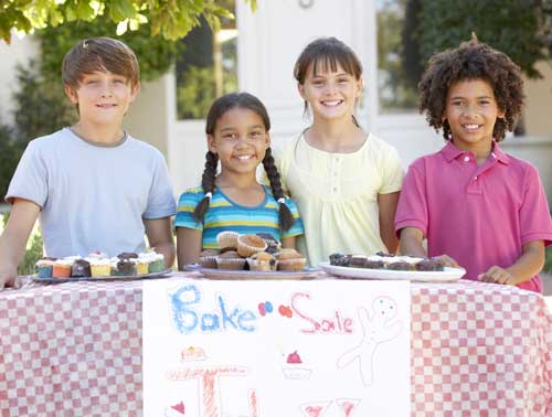A group of children outdoors behind a sign that says Bake Sale