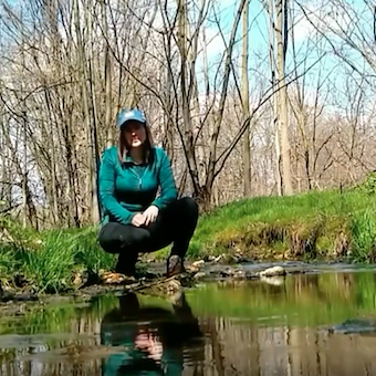 Liz Yocom kneels along a stream.