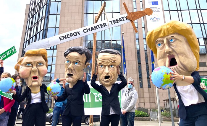 Demonstrators wear masks with the EU leaders under a sword that reads Energy Charter Treaty.
