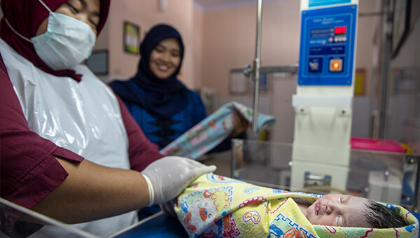 Local health workers swaddle a baby.